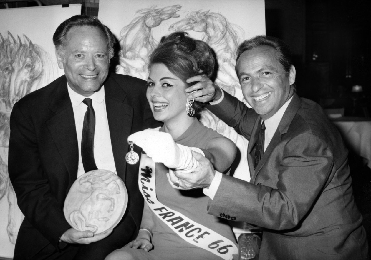 Rene Bollinger (venstre) og Guy Lux-entourent Monique Boucher «Miss France» til hvem de nettopp leverer inn en nøkkelring «Talisman Du Turfiste» under åpningen av Bollingers Canvas 12. juli 1966 av Unknown