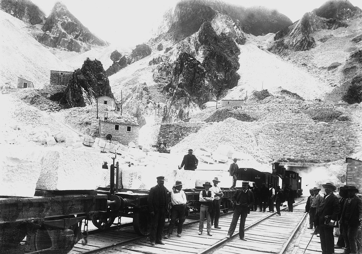 Gravemaskiner foran en jernbanekonvoi lastet med blokker av marmor ved Ravaccione, i Apuan-alpene (s/hv-bilde) av A. Corsini