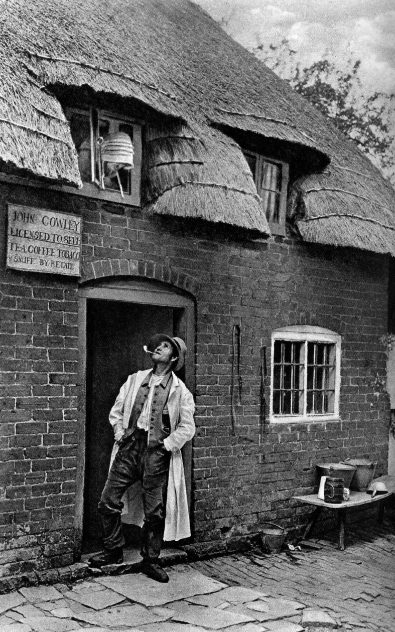 En mann røyker pipe utenfor en butikk, Worcestershire, c1922. av A. W. Cutler