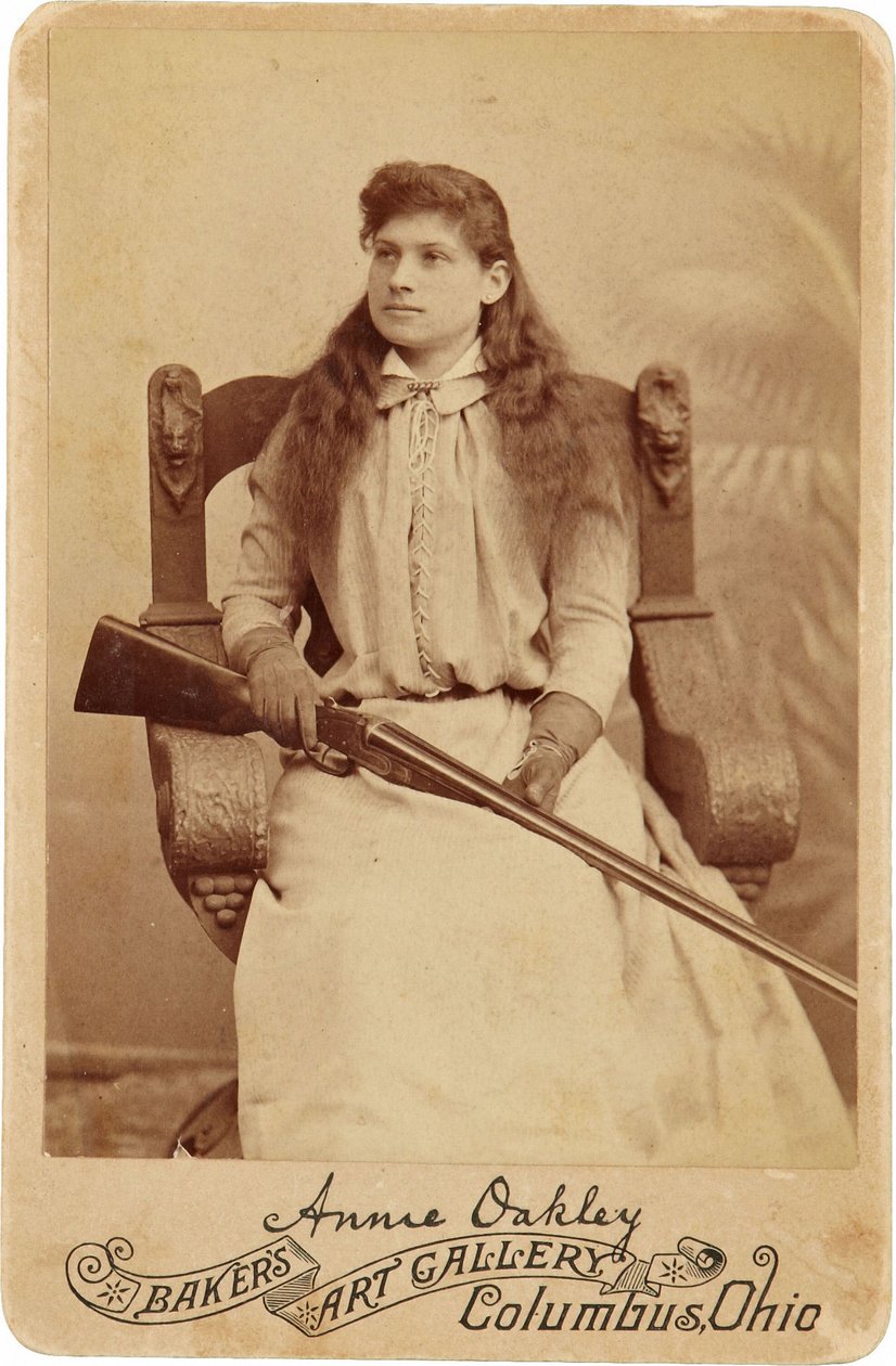 Annie Oakley: Annie Oakley:. Her sitter den legendariske skarpskytteren ganske nedverdig i en massiv stol i renessansestil, en hagle som hviler i fanget hennes. Hennes delikate feminine trekk og flytende hår motvirker hennes robuste utendørs bilde ©Buyenla av American Photographer