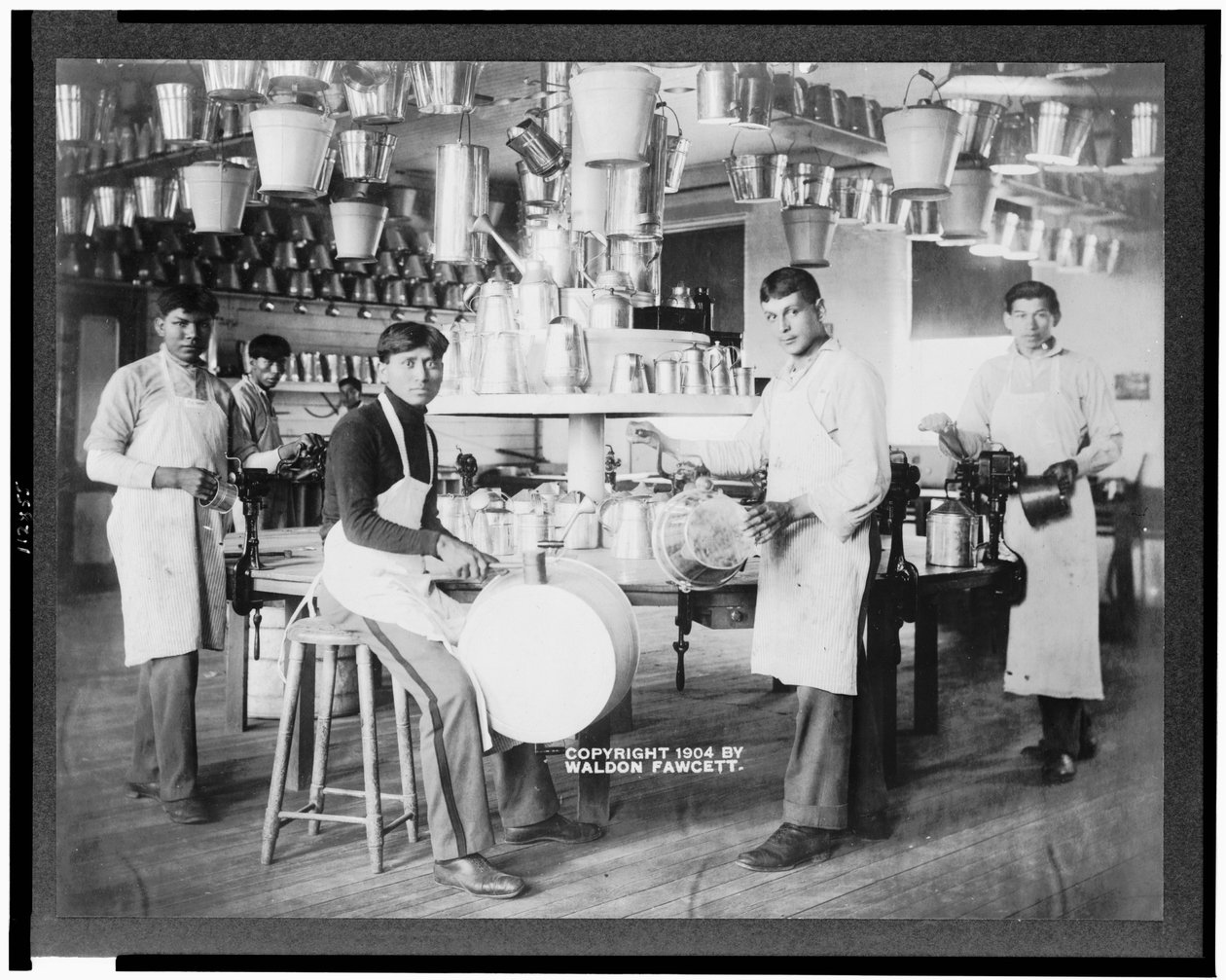 Unge indianermenn i metallbearbeidingsverksted med spann, vaskekar, vannkannere og andre metallgjenstander, Carlisle Indian School, Pennsylvania, ca. 1904 (s/hvitt-bilde) av American Photographer