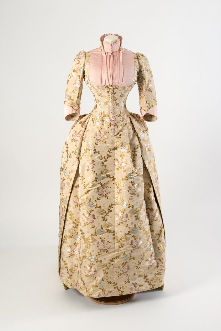 Kjole av lysebrun silke vevd med et design av lilla, blå og gule blomster og grønne blader, lys rosa ribbet silkeoverdel og mansjetter av American School
