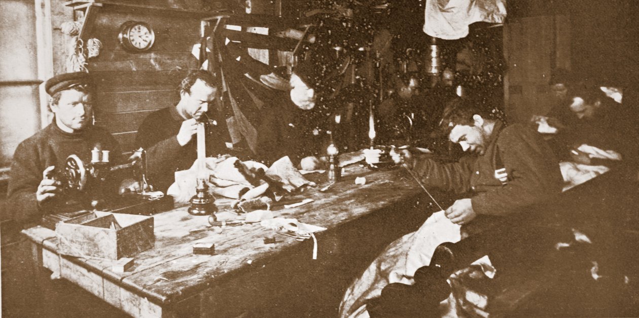 I hytta midtvinteren drev mennene med å sy pelsverk til klær som skulle brukes til aking på våren, pub. London 1907 (s/hvitt-bilde) av Anthony Fiala