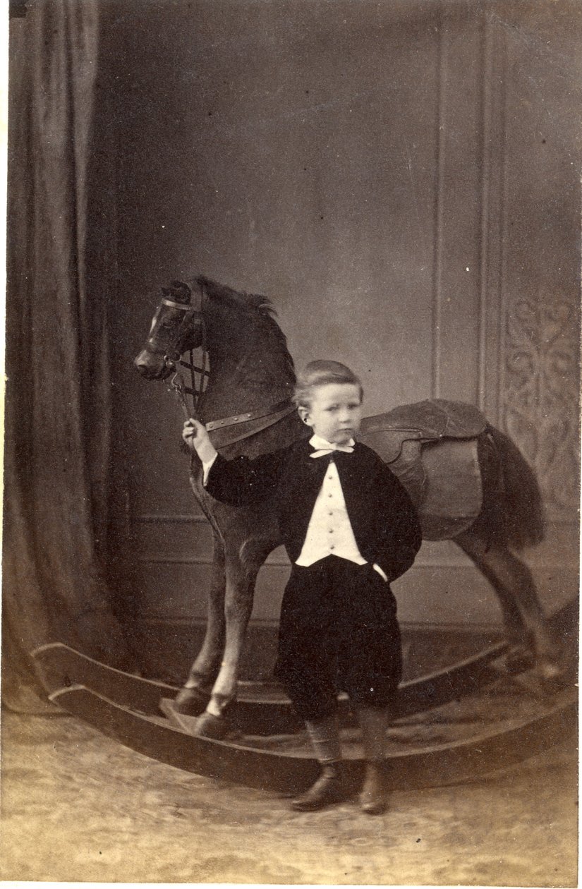 Gutt som står og holder tøylene til en gyngehest, 1860-tallet (albumintrykk) av Barat