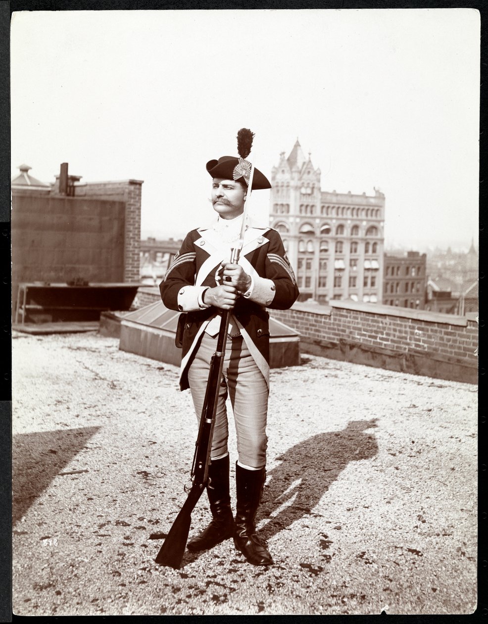 En mann på et tak kledd i en tradisjonell militæruniform, holder en rifle, 1895 (sølv gelatintrykk) av Byron Company