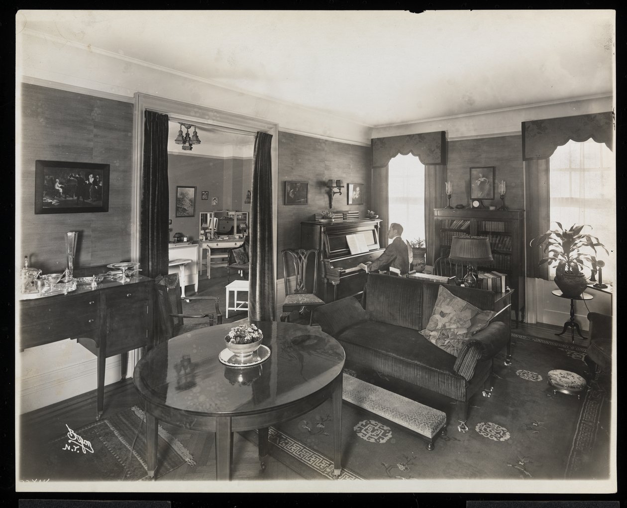En mann som spiller piano i en stue i A.C. Cronin-residensen, 1915-16 (sølv gelatintrykk) av Byron Company