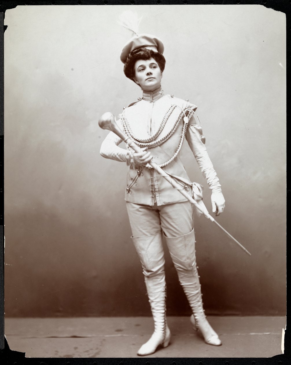 En kvinne som modellerer en banduniform og holder en stafettpinnen, ca. 1898 (sølv gelatintrykk) av Byron Company