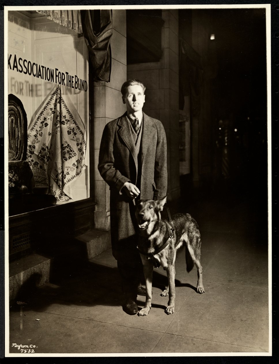 Blind mann og førerhunden hans på fortauet foran New York Association for the Blind, 111 East 59th Street, New York, 1938 (sølv gelatintrykk) av Byron Company