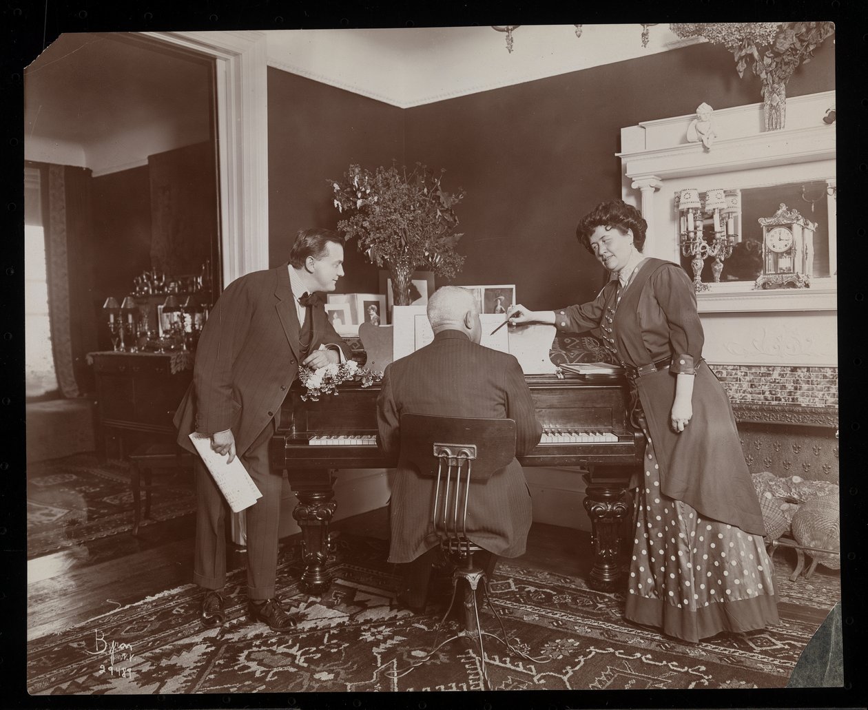 Clara De Regand peker på et partitur mens en mann spiller piano, 1910 (sølv gelatintrykk) av Byron Company