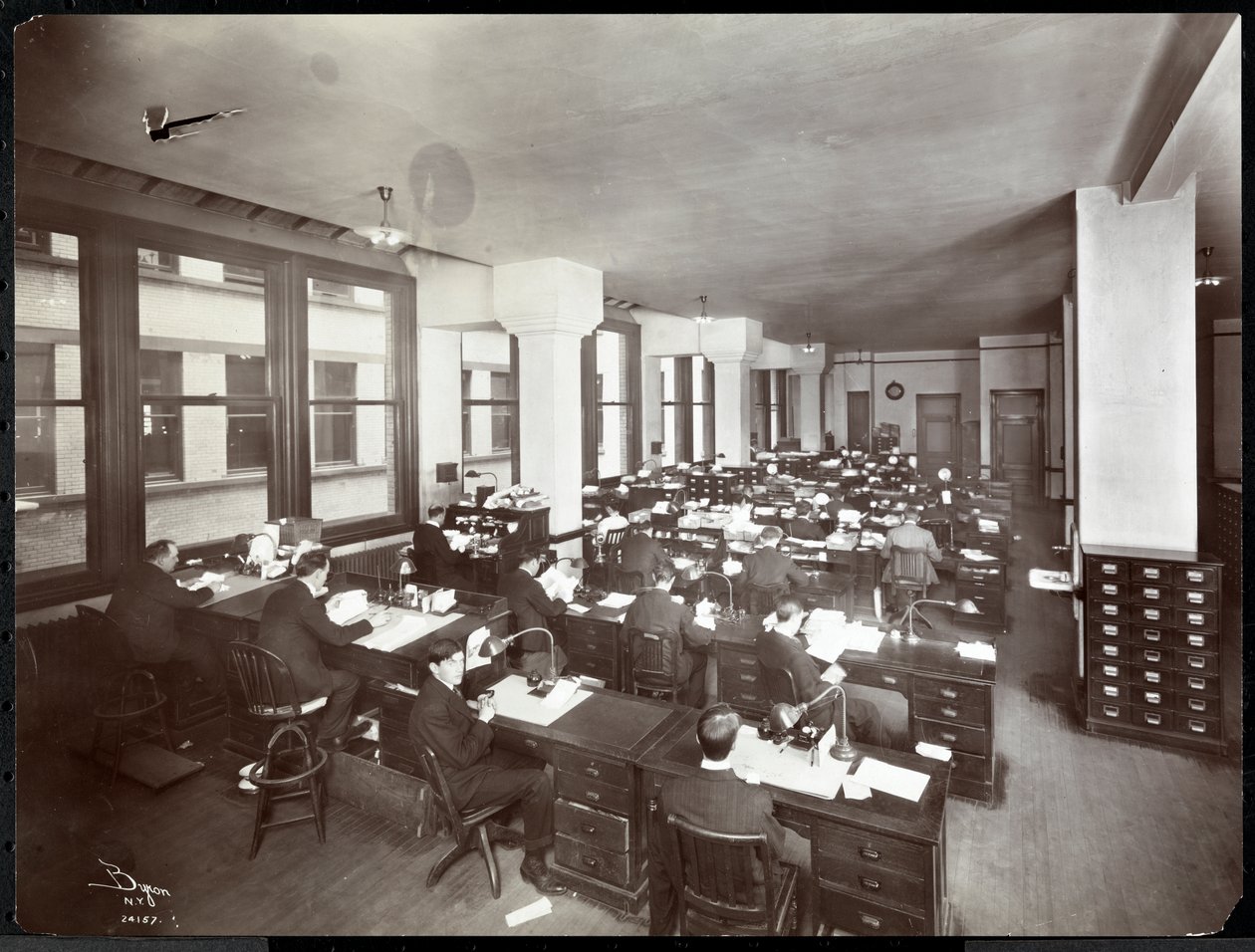 Menn og en kvinne som jobber ved pulter på et kontor hos Metropolitan Life Insurance Co. på 23rd Street og Madison Avenue, New York, 1907 (sølv gelatintrykk) av Byron Company