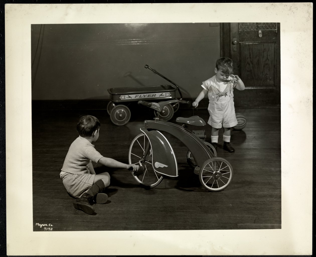 To blinde synshemmede gutter som leker med en trehjulssykkel og rød vogn ved New York Association for the Blind, 111 East 59th Street, New York, 1937 (sølv gelatintrykk) av Byron Company