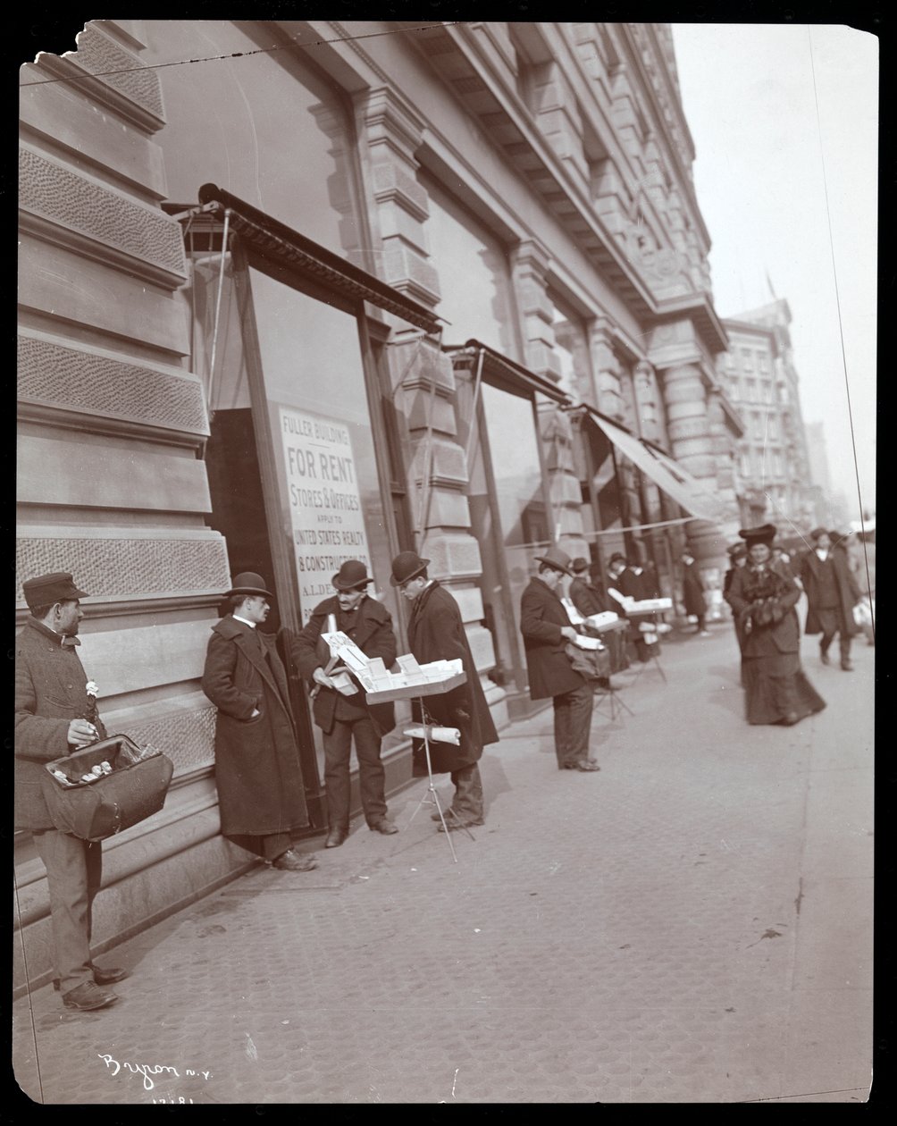 Utsikt over kjøpmenn som selger leker og andre gjenstander foran Fuller- eller Flatiron-bygningen på Broadway, 5th Avenue og 23rd Street, New York, ca. 1895 (sølvgelatintrykk) av Byron Company