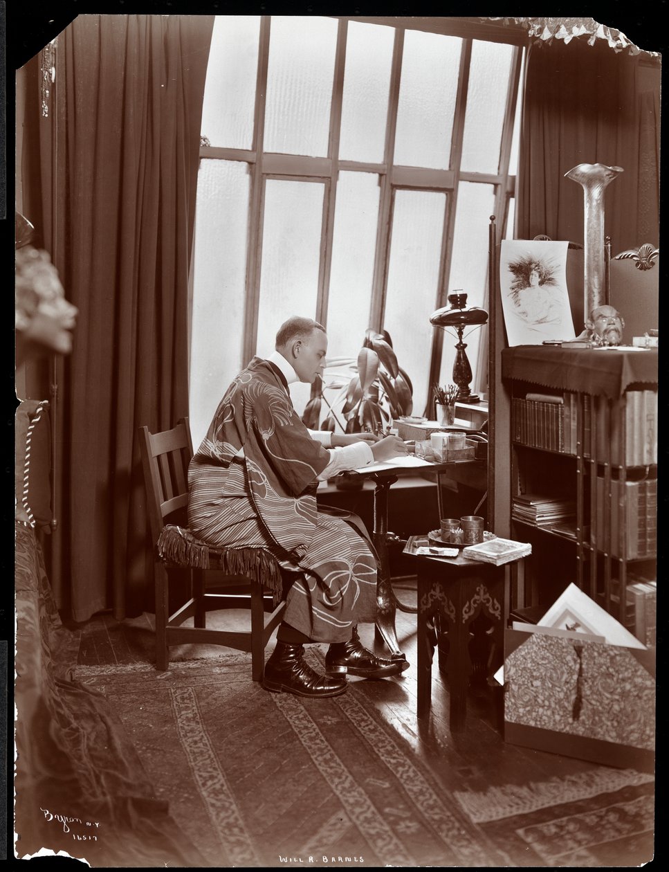 Will R. Barnes i en kappe, sittende ved skrivebordet i studioet hans, 1903 (sølv gelatintrykk) av Byron Company