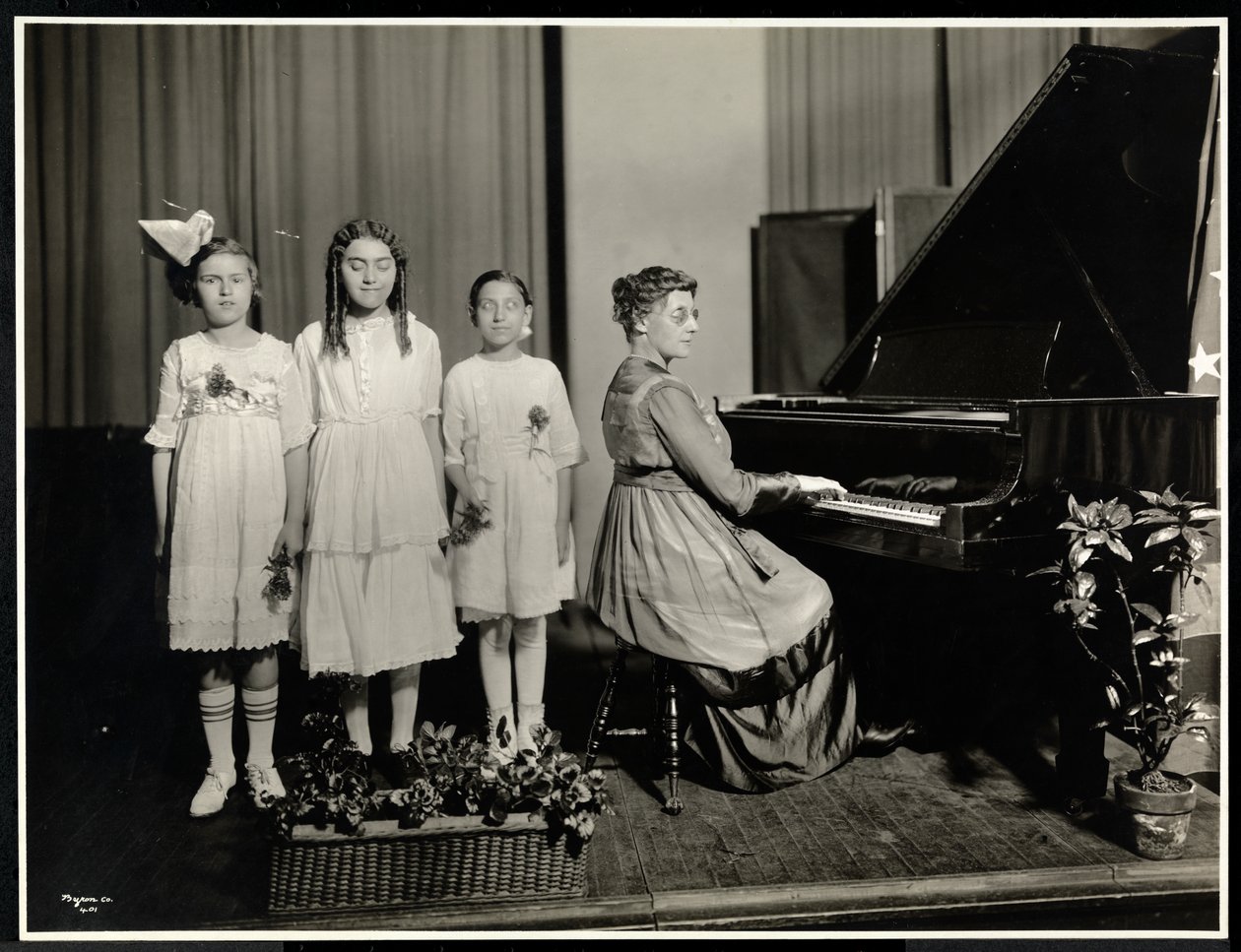 Kvinne som spiller piano mens tre jenter synger i New York Association for the Blind, 111 East 59th Street, New York, ca. 1917 (sølv gelatintrykk) av Byron Company