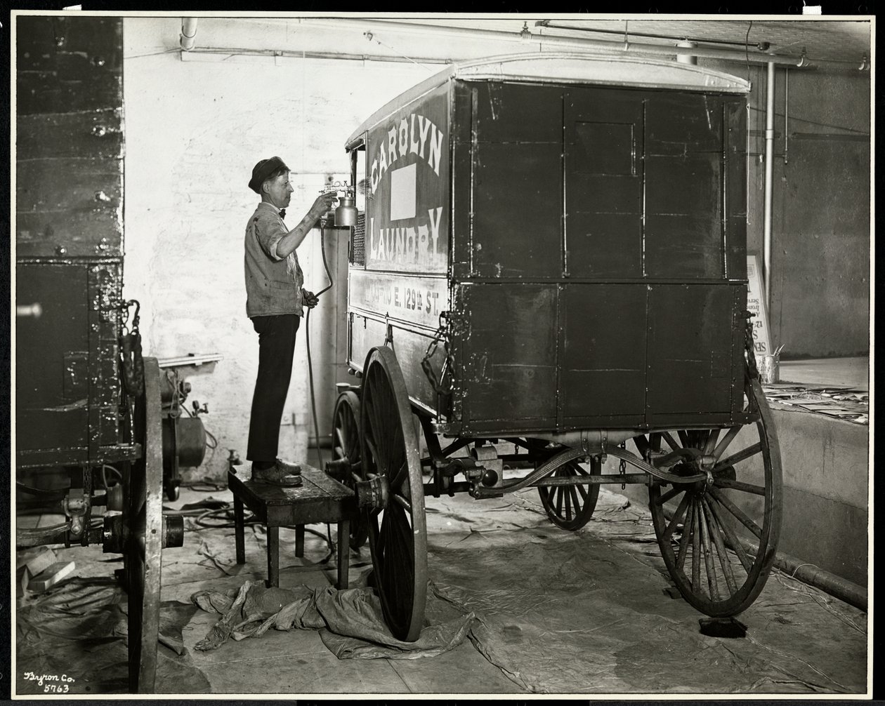 En mann som spraymaler en leveringsvogn fra Carolyn Laundry på 111 East 128th Street, East Harlem, New York, 1929 (sølv gelatintrykk) av Byron Company