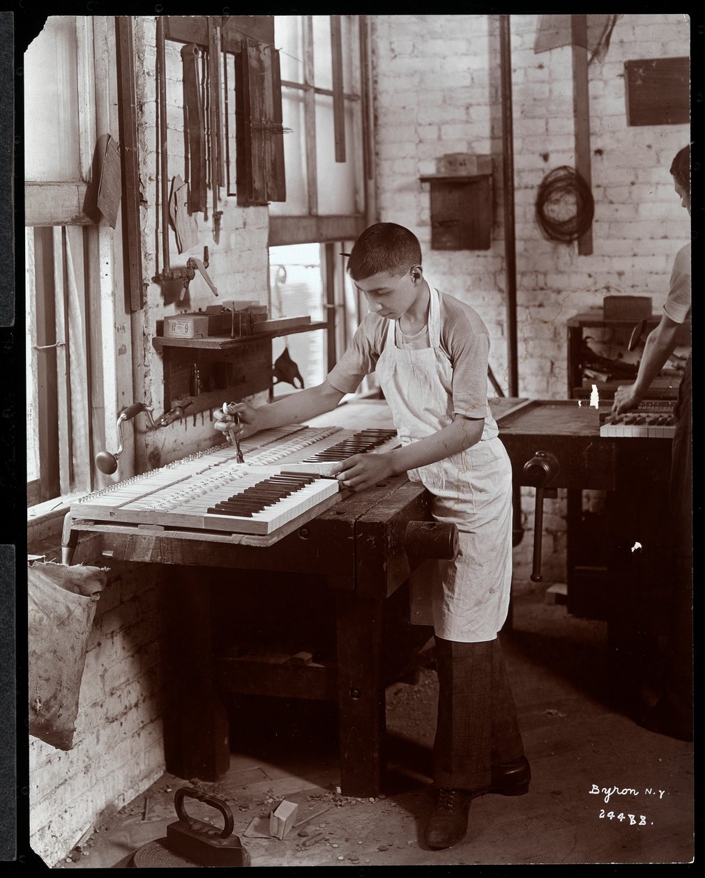 En ung mann som arbeider i Harrington Piano Co.-fabrikken, 1907 (sølv gelatintrykk) av Byron Company