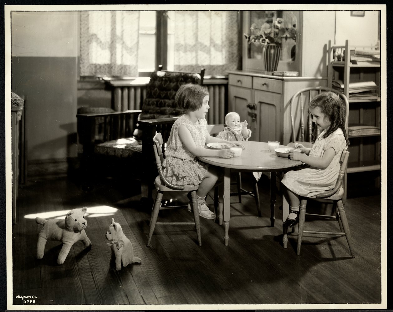 To blinde synshemmede jenter spiser ved et lite bord med dukke hos New York Association for the Blind, 111 East 59th Street, New York, 1933 (sølv gelatintrykk) av Byron Company