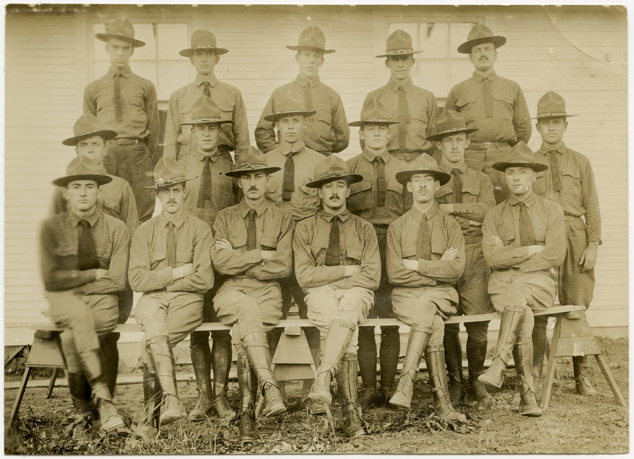 Horisontalt sepia -fotografi som viser en gruppe på sytten uniformerte soldater som poserer for et gruppebilde. Soldatene er delt inn i tre rader; en rad sittende foran, en rad stående i midten og en rad på en plattform i ba av Carl Michel