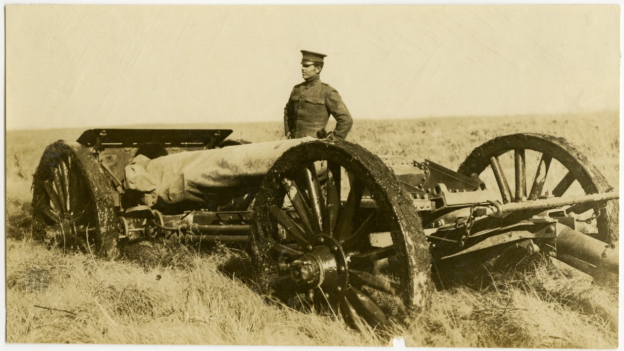 Horisontalt, sepia -fotografi som viser en uniformert mann som står ved siden av en artilleripistol på hjul i et åpent felt av Carl Michel