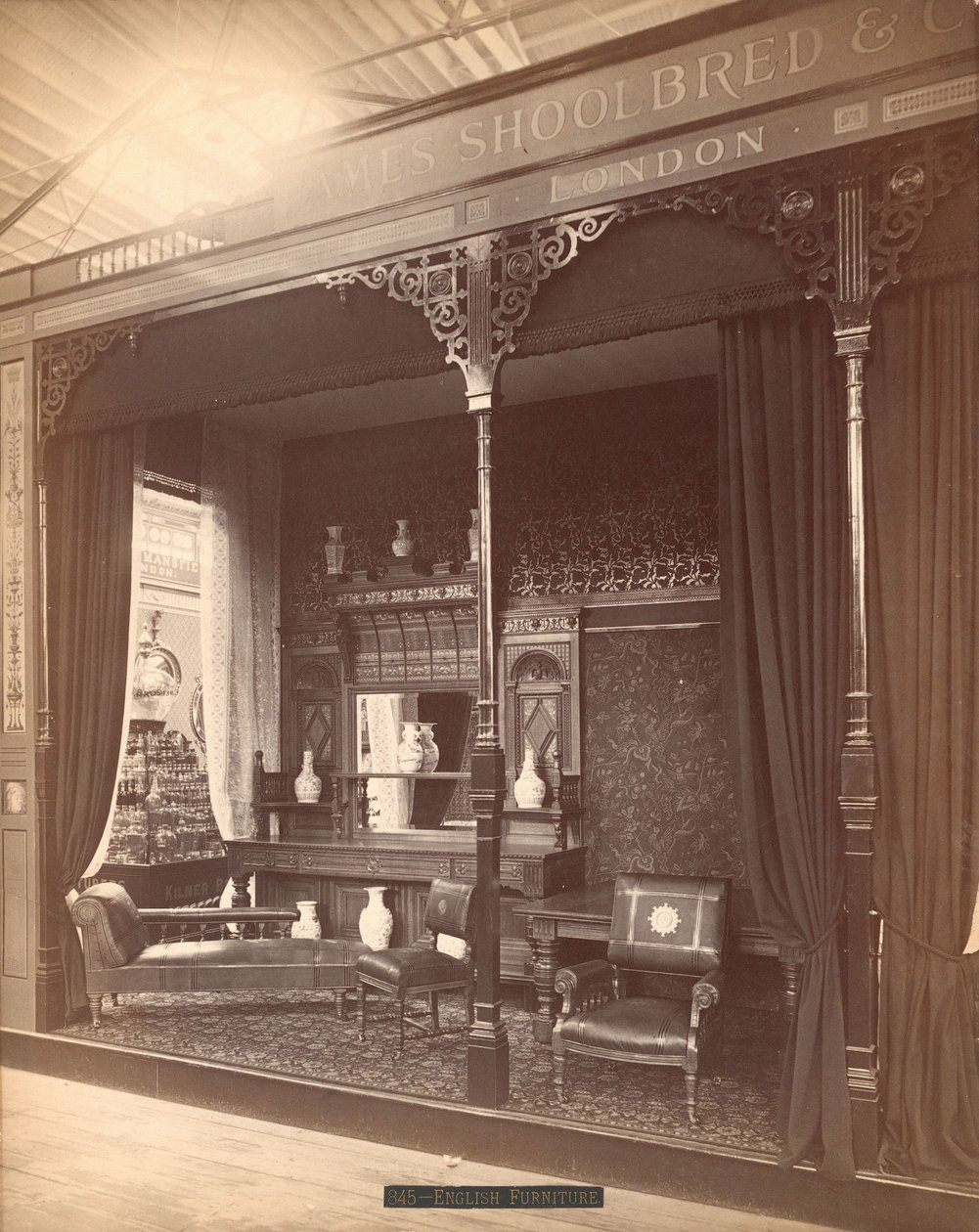 James Shoolbred & Co.s utstilling -- Hovedbygning, Parlor-scene bestående av en skjenk og speil med vaser på og foran, stoler, et bord og en sofa. På gulvet ligger et teppe og veggene er dekket av blomstertapet av Centennial Photographic Co.