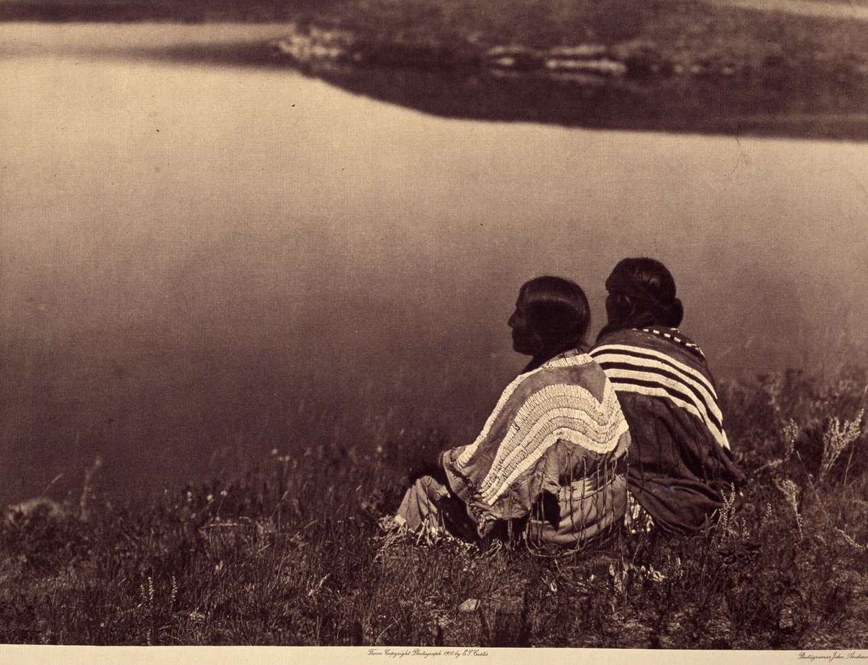 En ledig time - Et øyeblikk av ro: Piegan-indianere som sitter på kanten av en vannmasse. Foto hentet fra bind 6 av leksikonet utgitt av Edward S. Curtis (1868-1952) om indianerne i Nord-Amerika, med et forord av Theodore Roosevelt. B av Edward Sheriff Curtis
