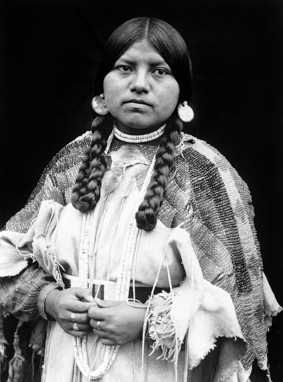 Cayuse kvinne, halvlangt portrett, stående, vendt forover, fletter, skjellskiveøredobber, skallperler og skallperler rundt halsen, perlekledd bukkskinnskjole med perlebelte c. 1910, foto Edward S. Curtis av Edward Sheriff Curtis