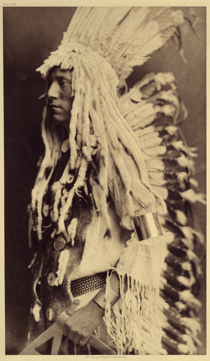 Gammel person, Piegan. Unge menn går ikke glipp av noen anledninger til offentlige festligheter for å ta på seg klærne til sin krigerfar. Foto hentet fra bind 6 av leksikonet utgitt av Edward S. Curtis (1868-1952) om indianerne i Nord-Amerika, med en forgr av Edward Sheriff Curtis