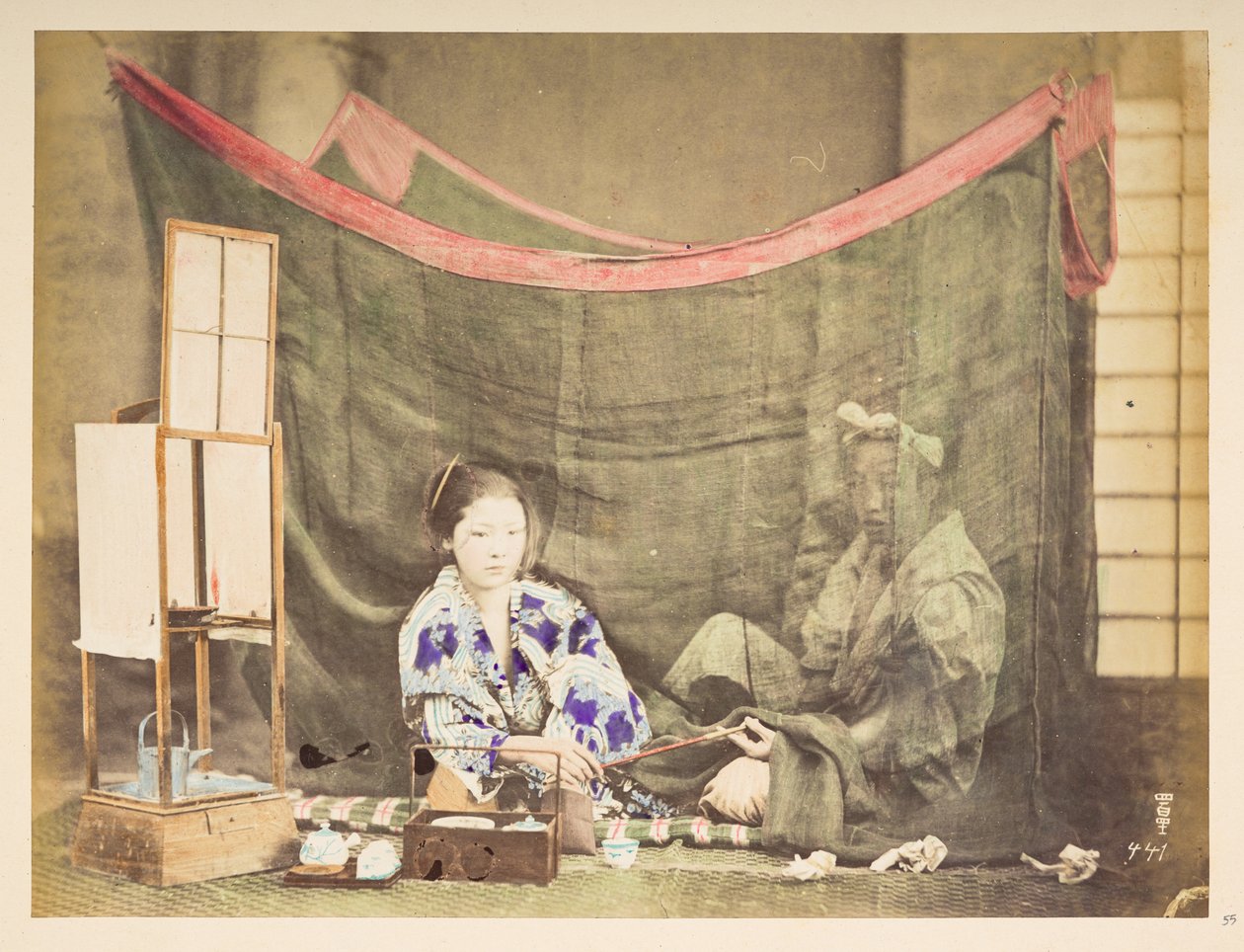 japansk par på fritiden, Studio-tableau av en ung japansk kvinne, sittende med tekokende hindring rundt seg, og gir en pipe til en mannsfigur som sitter bak henne, skjermet av et linmyggnett,   Fotograf: Ukjent  Lucas samling: av English Photographer