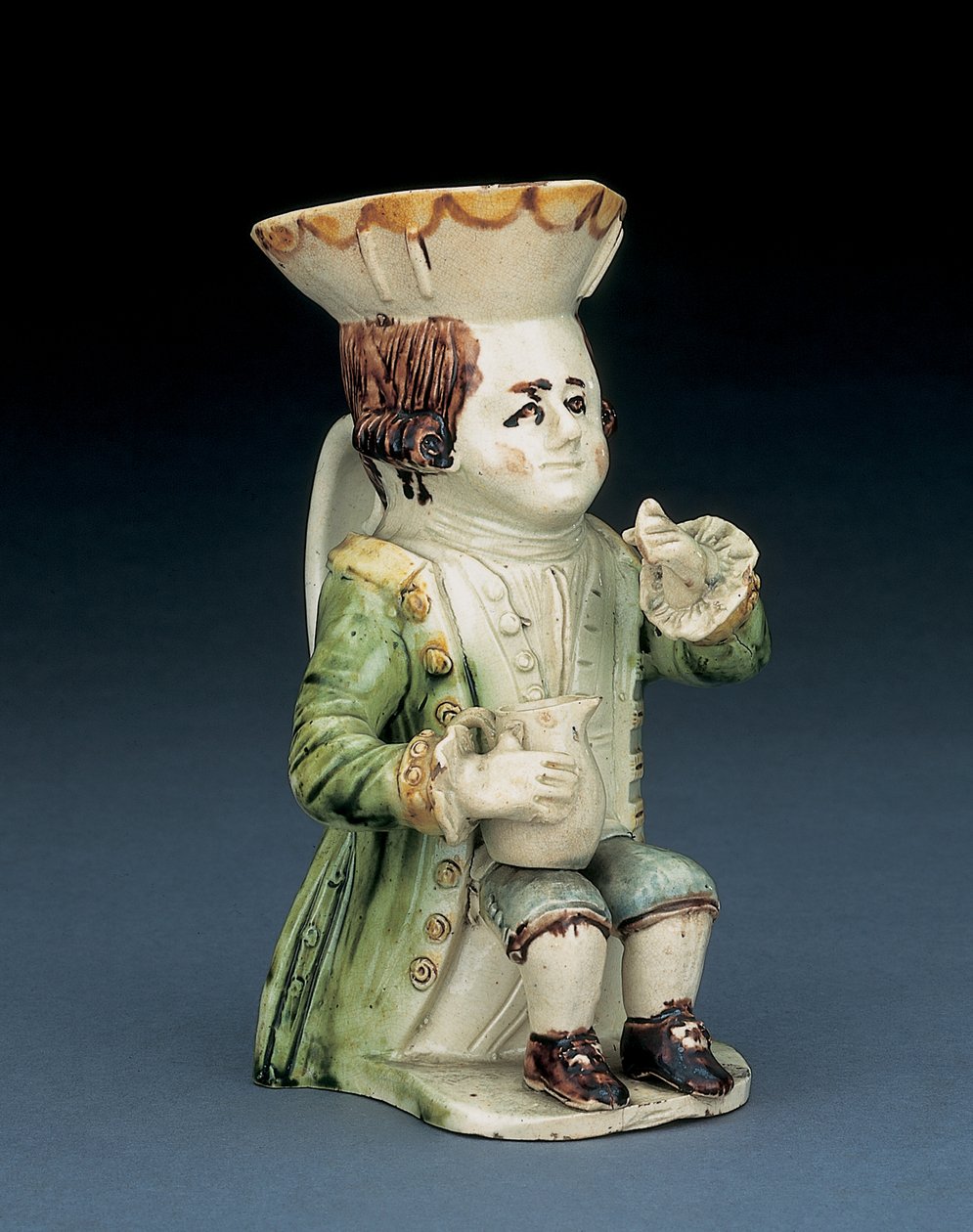 Toper toby kanne, hatten hans med brun og gul kamkant, det innskårne brune håret i kø og med en hvit rosett sittende med en baluster kanne på kneet, ca. 1770 av English School