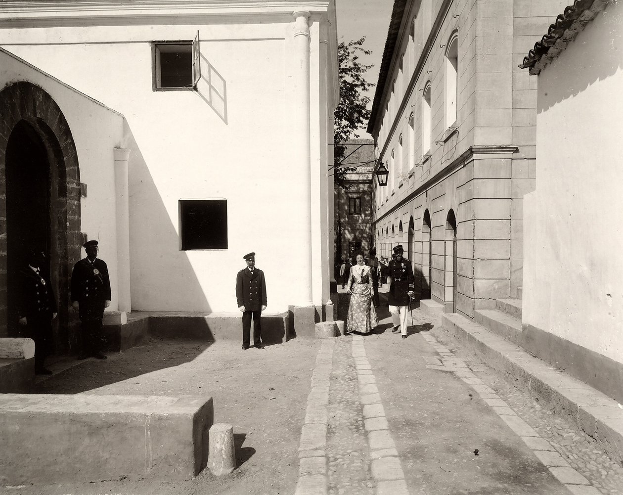 Menn i uniform følger en elegant kledd kvinne mot kirken til gården Lo Zucco, Sicilia, 1900 av Eugenio Interguglielmi
