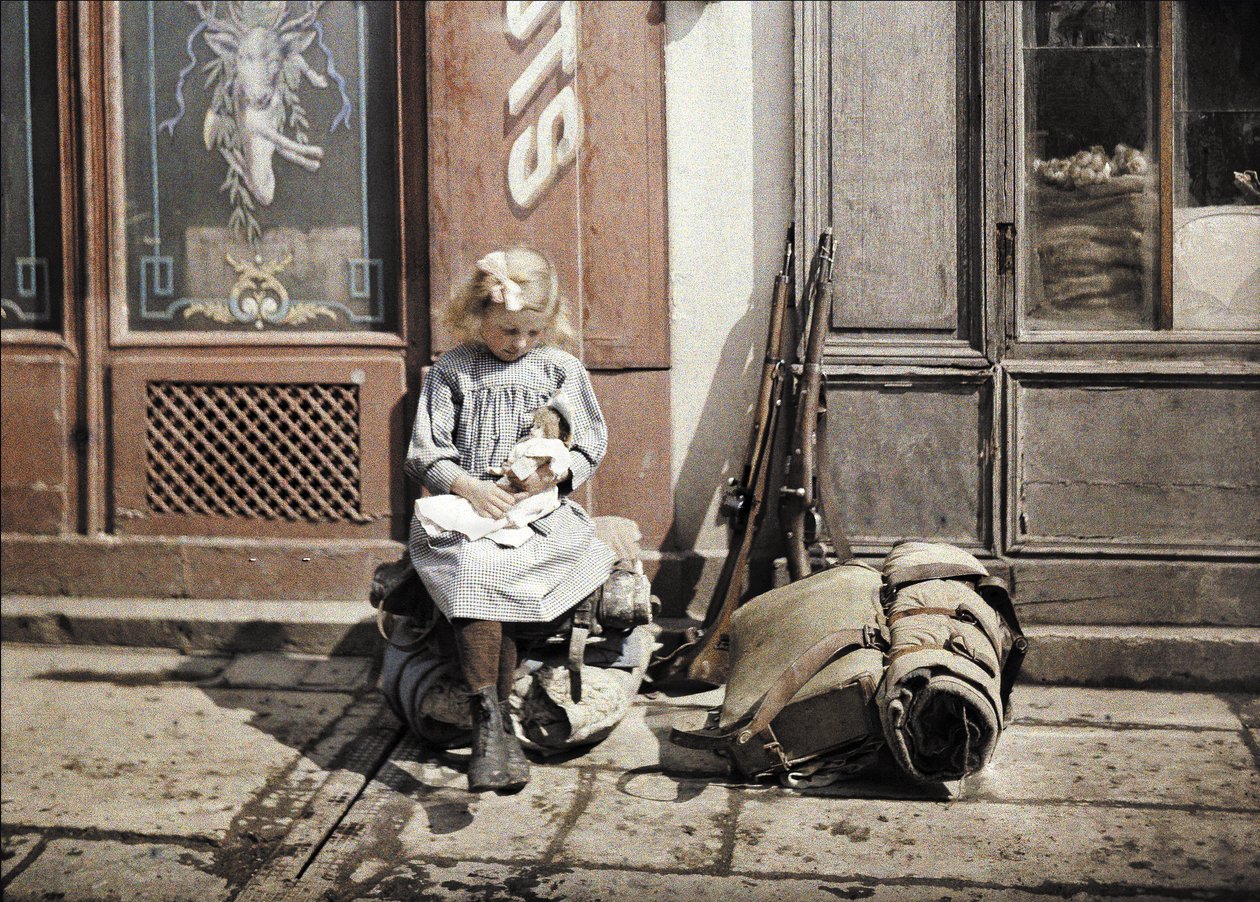 En liten jente som leker med dukken sin; to våpen og en ryggsekk er ved siden av henne på bakken, Reims, Marne, Frankrike, 1917 (autokrom) av Fernand Cuville