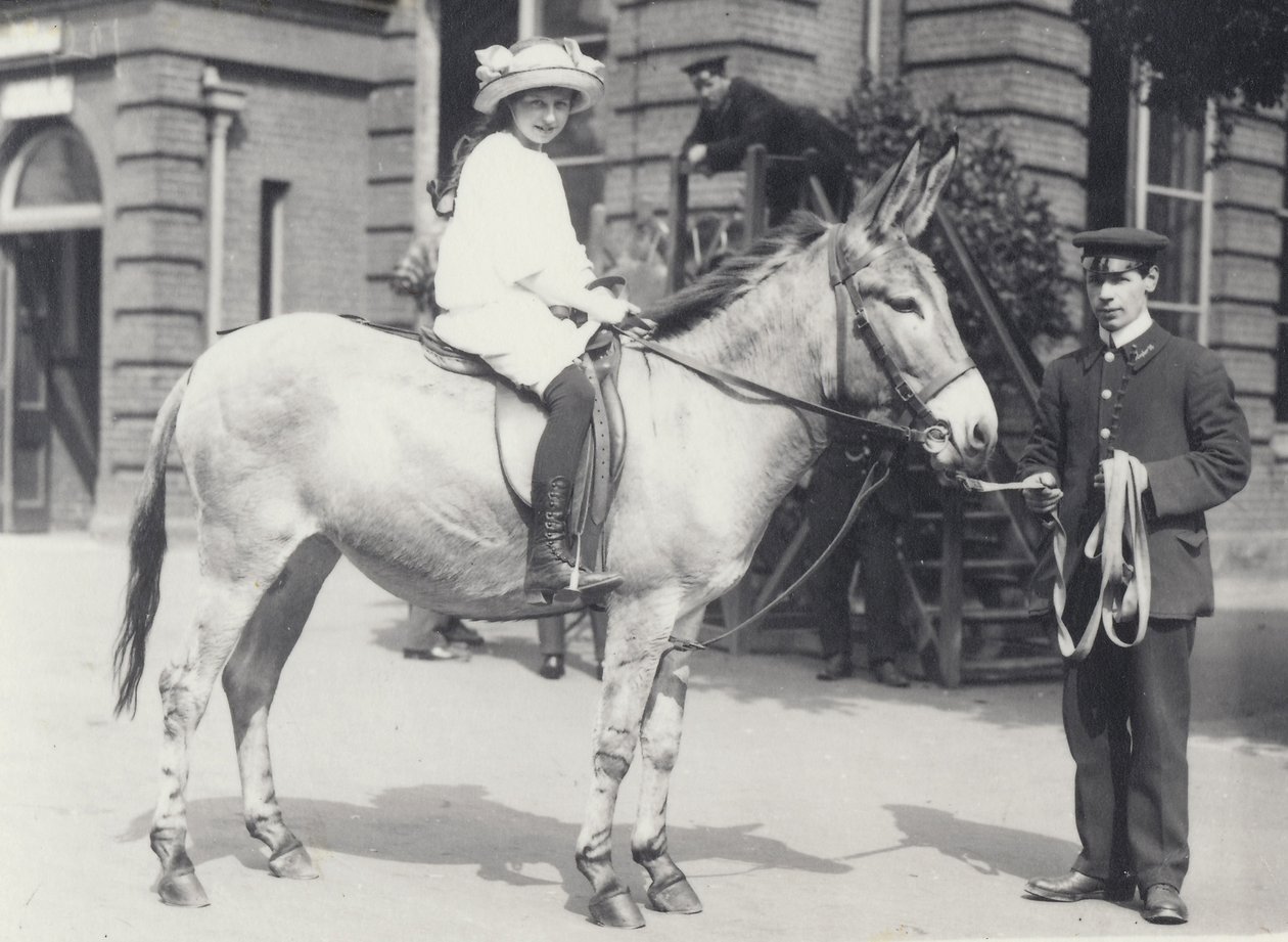 En ung dame som rir på en rumpe som blir ledet av en keeper mens en annen ser på, London Zoo mai 1914 av Frederick William Bond