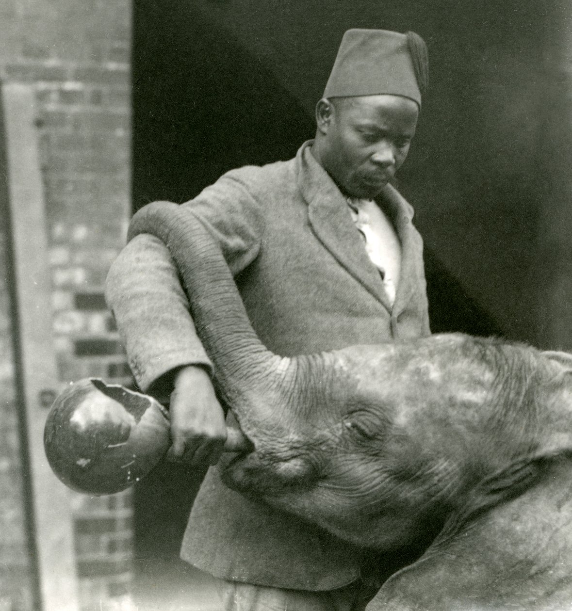 Den unge afrikanske elefanten Kiberenge får en drink av Darisha mens Syed Ali ser på i bakgrunnen, London Zoo, september 1923 (bw-bilde) av Frederick William Bond