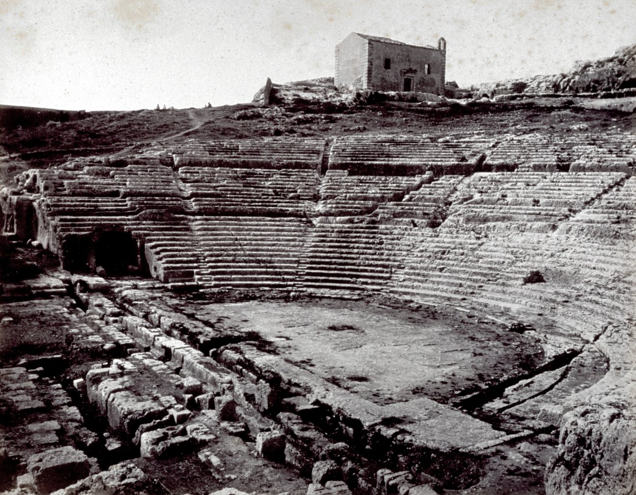 Restene av det greske teatret i Siracusa i den monumentale parken i Neàpoll. I forgrunnen det halvsirkelformede orkesteret og caveaen av Giorgio Sommer