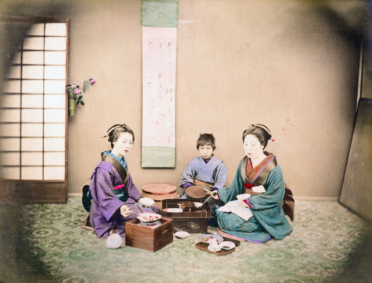 To kvinner og et barn spiser lunsj, sittende på en matte, ca. 1890 (håndfarget bilde) av Japanese Photographer