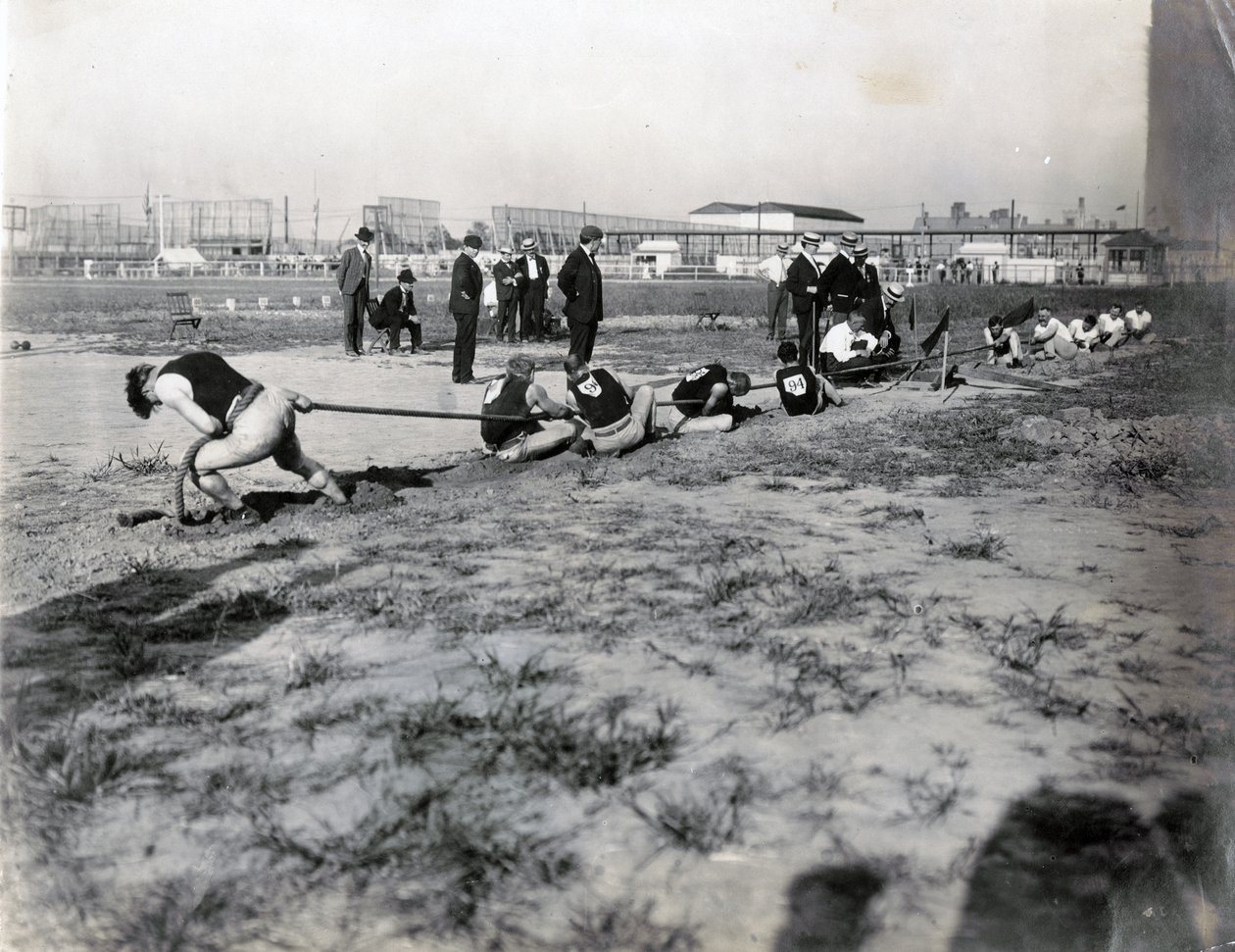 Horisontalt fotografi av to lag som konkurrerer i dragkamp. Det er dommere som står bak tauet. Skyggene til tilskuere kan sees på fotografiet av Jessie Tarbox Beals