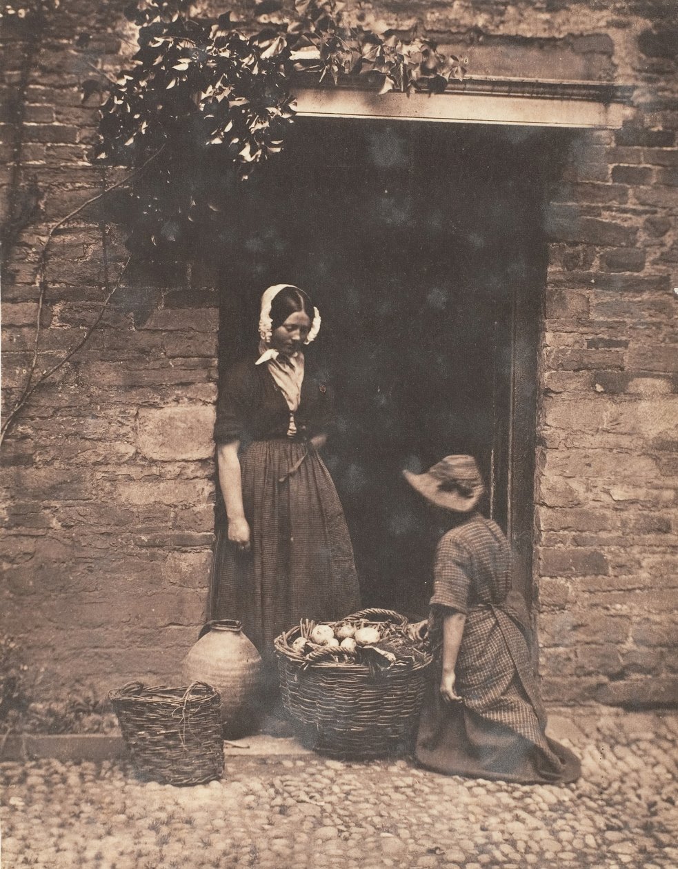 [To kvinner, en knelende og en stående, ser inn i kurv fylt med grønnsaker], 1853-56. av John Dillwyn Llewelyn