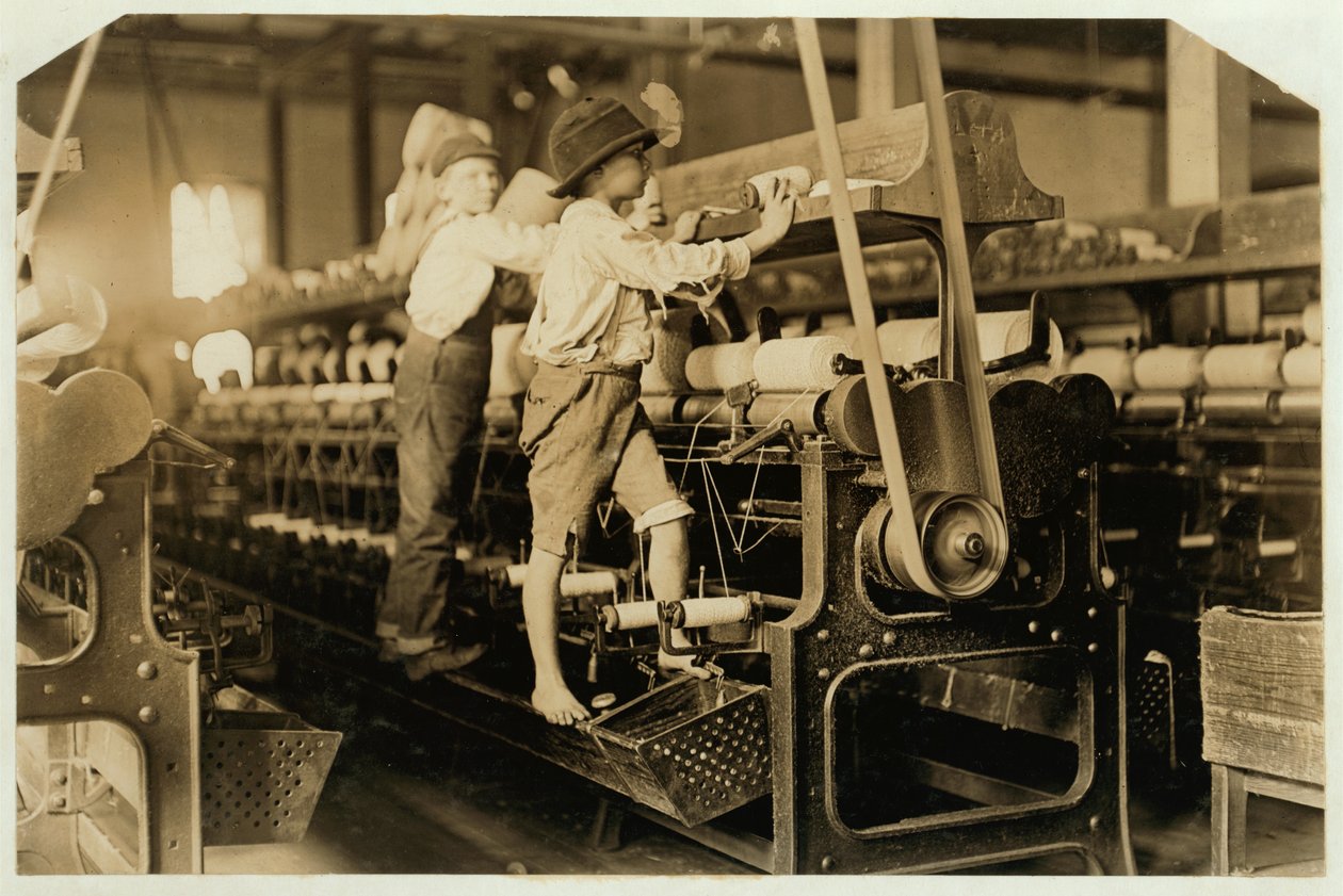 Små gutter som klatrer på spinnende ramme for å reparere ødelagte tråder og erstatte tomme spoler ved Bibb Mill, Macon, Georgia, 1909 av Lewis Wickes Hine