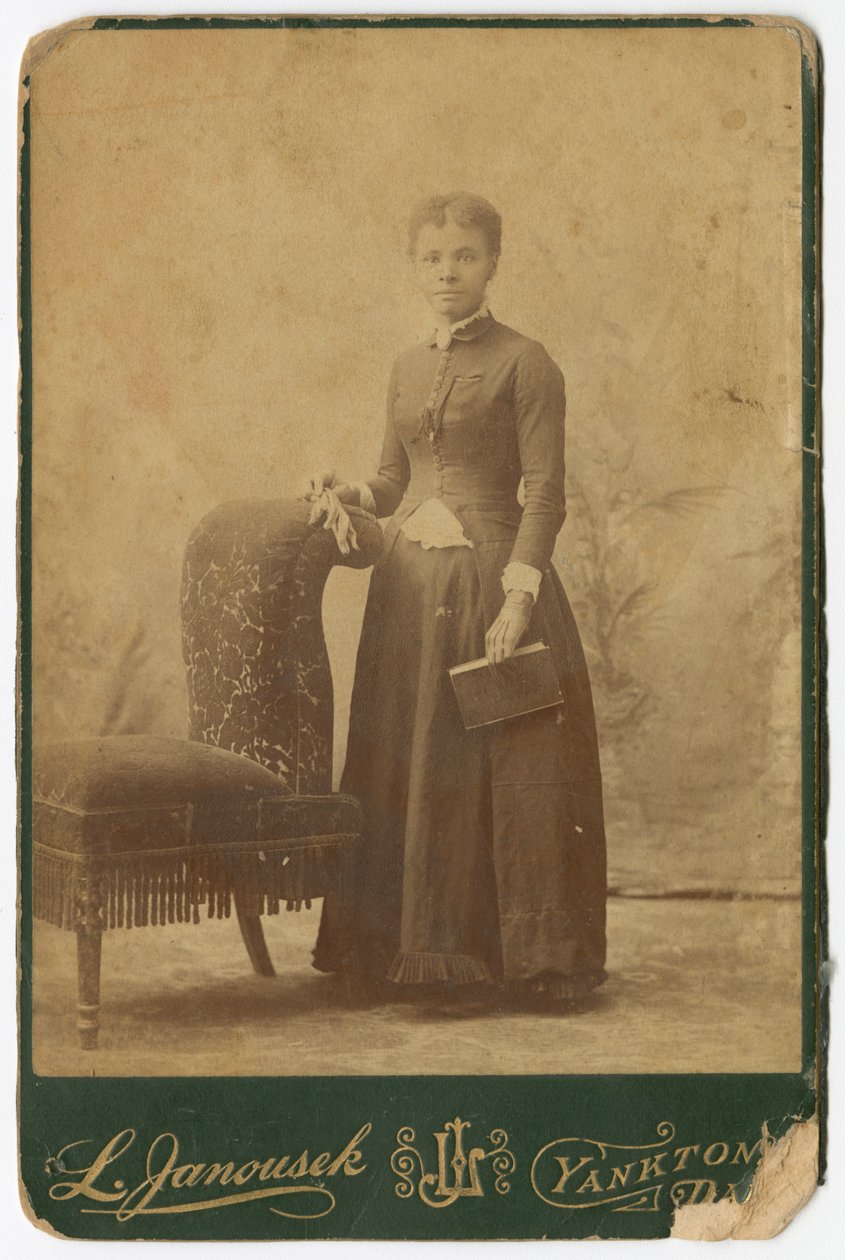 Fotografi av en kvinne som står ved siden av en stol og holder en bok, sent på 1800-tallet. av Louis Janousek