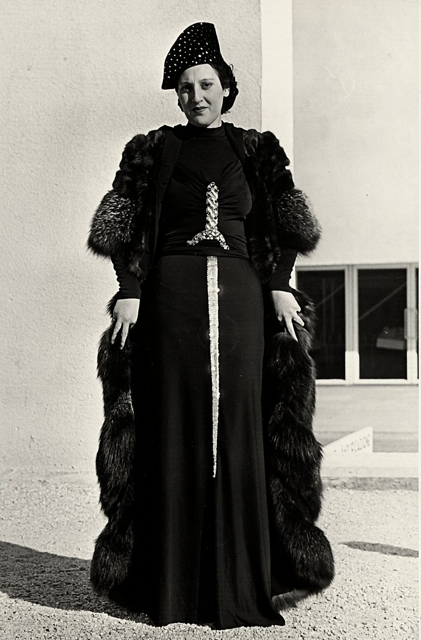 Modell i kveldskjole skapt av det italienske couturehuset "Dragoni". Skriften på artikkelen har en prangende paljettdekor i form av et sverd. En lue og pelsfrakk fullfører ensemblet. (s/hvitt bilde) av Luis Bogino