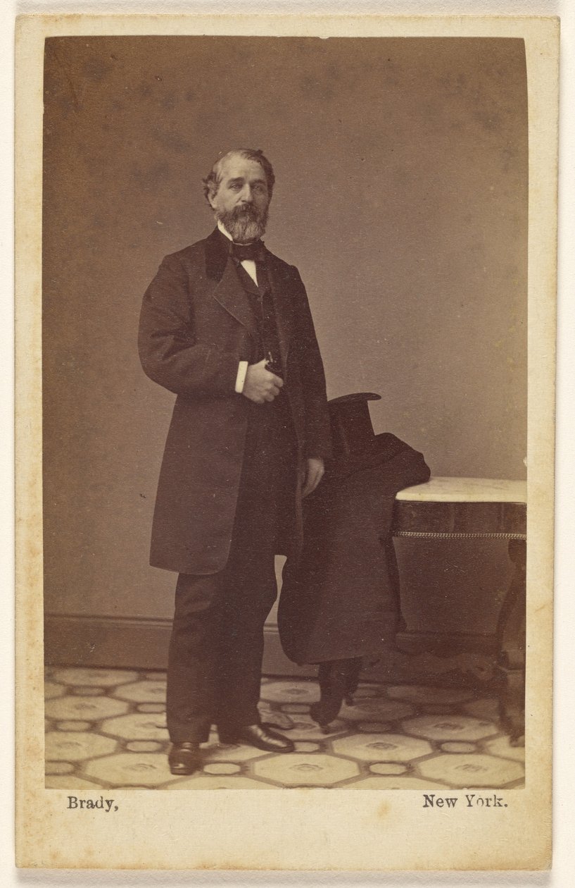 [Uidentifisert stående skjeggete mann, flosshatt og frakk på et nærliggende bord] av Mathew B. Brady