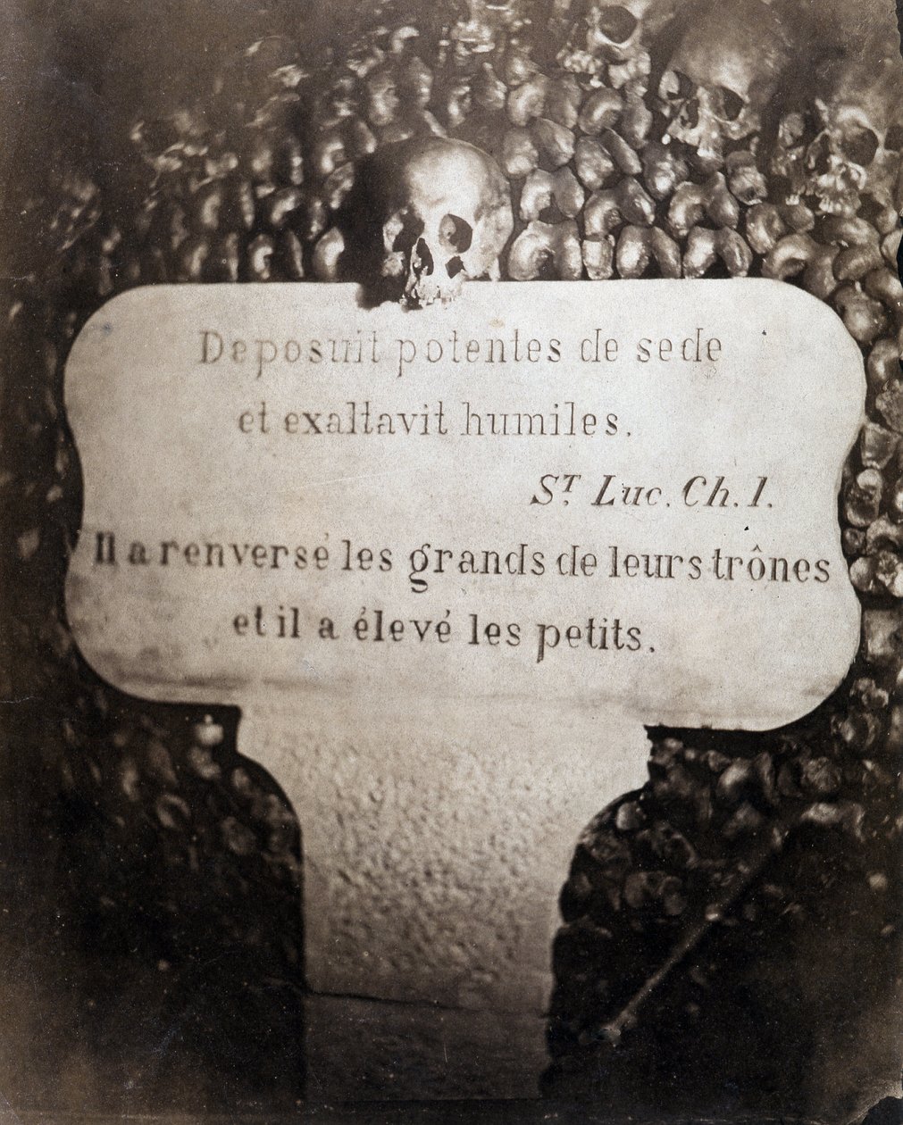Ossuariene til katakombene i Paris. Peter bærer et sitat fra kapittel 1 i Lukas-evangeliet (Deposuit potentes de sede et exaltavit humiles. På fransk: Han styrtet de store og reiste de små) av Nadar