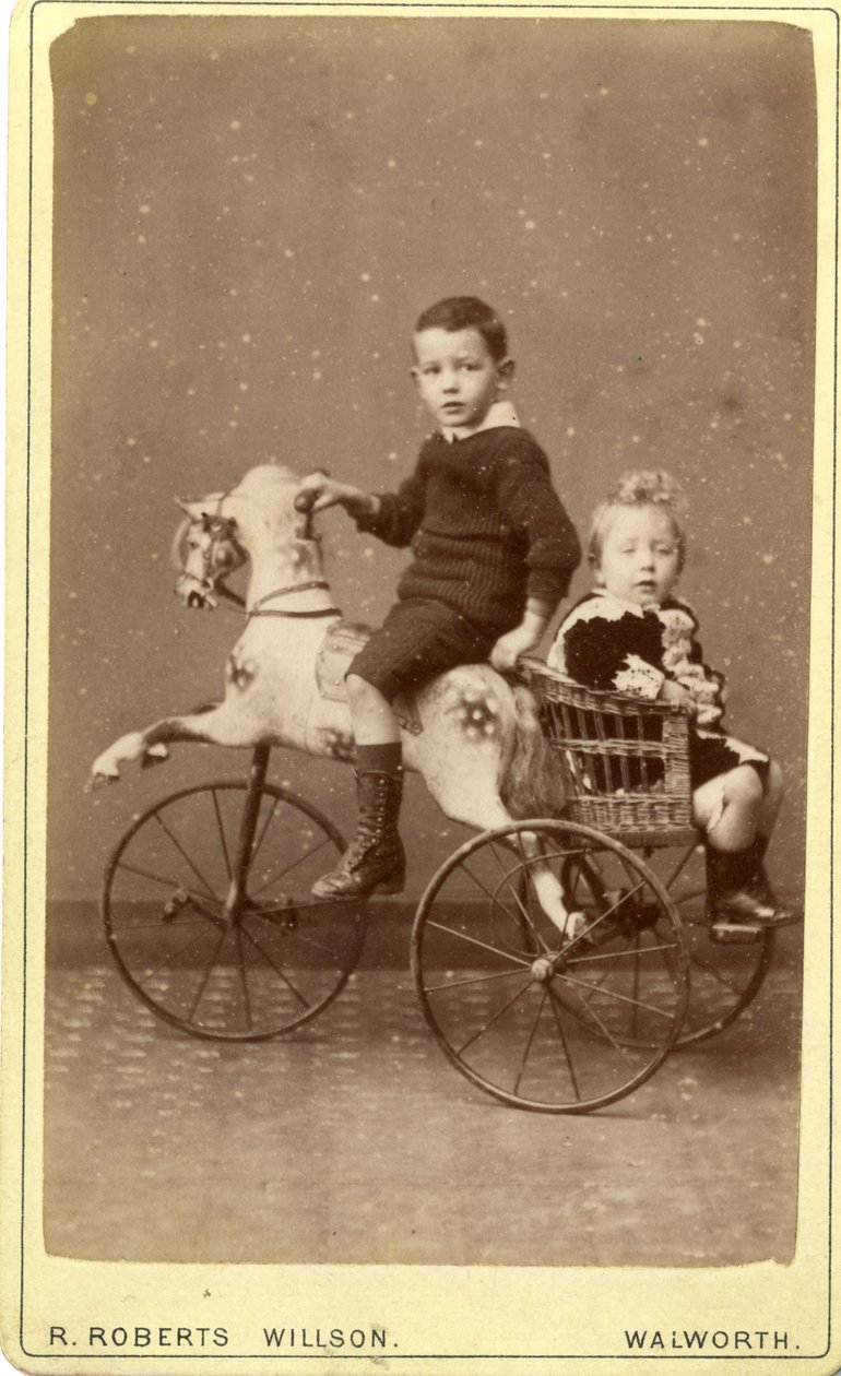 Ung gutt på gyngehest med ung jente i flettet vogn bak, 1880-tallet (albumintrykk) av R. Roberts Willson