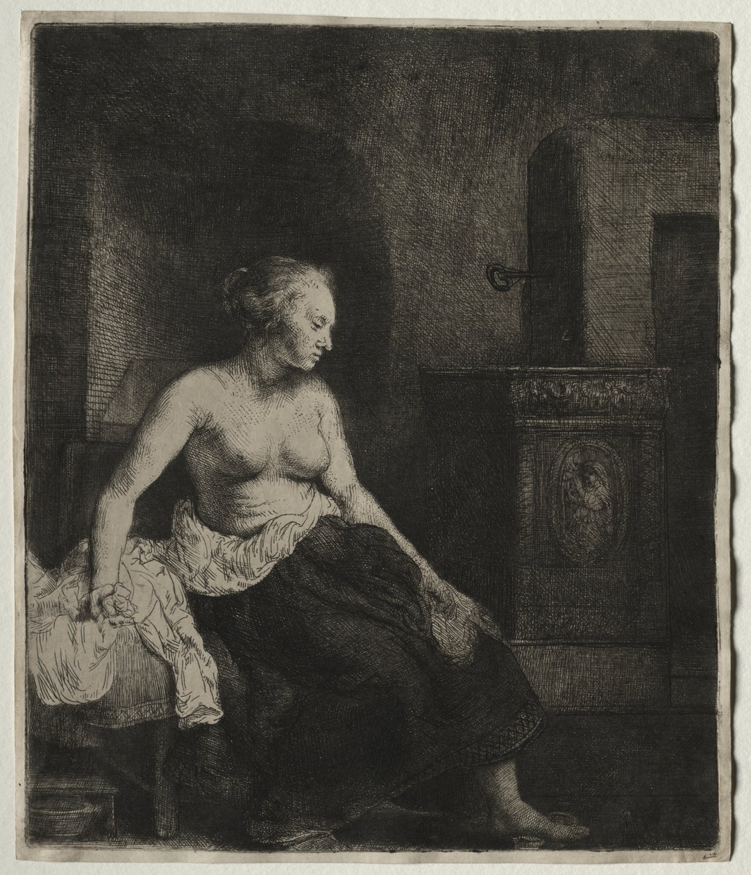 Kvinne som sitter halvkledd ved siden av en komfyr av Rembrandt van Rijn