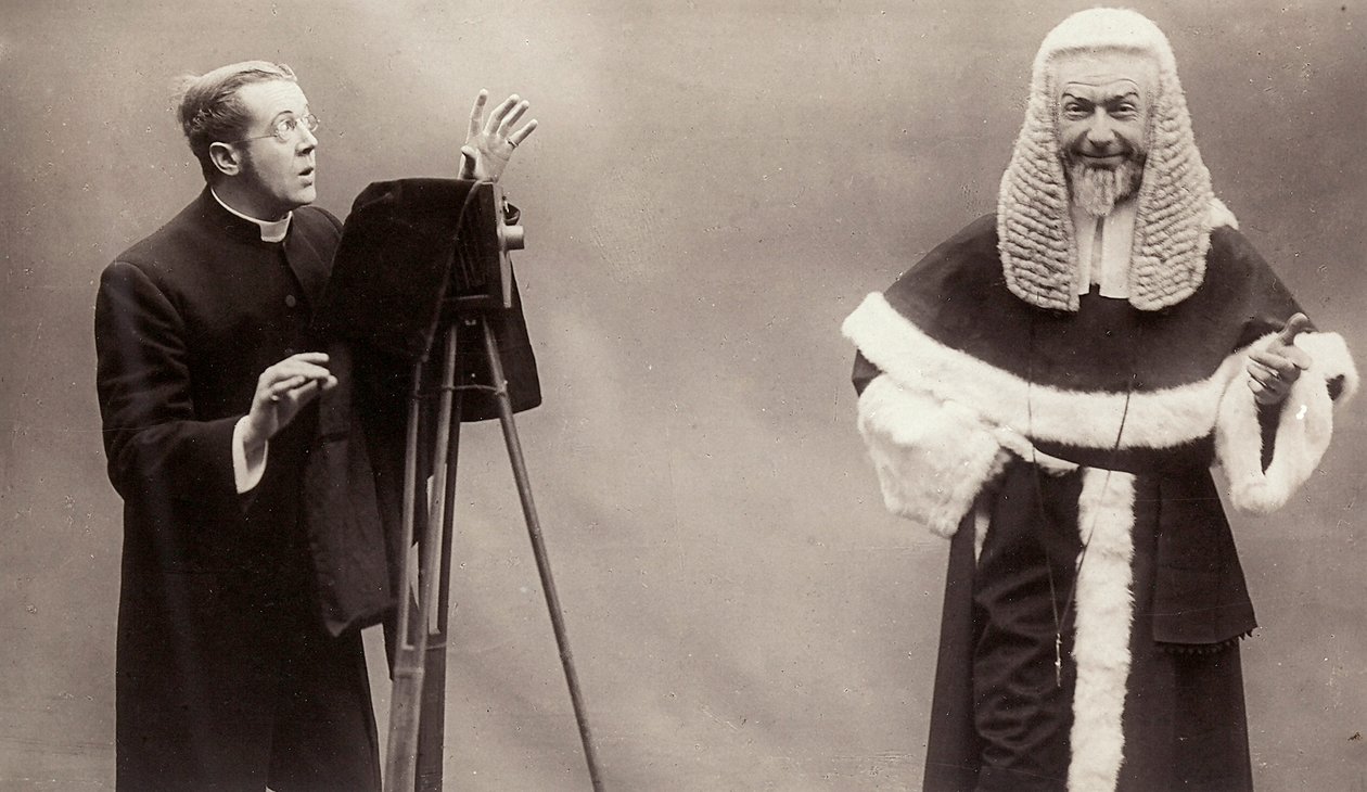 En mann i en sokk retter linsen på kameraet mot en mann kledd som en pave av Rotary Photographic Co Ltd