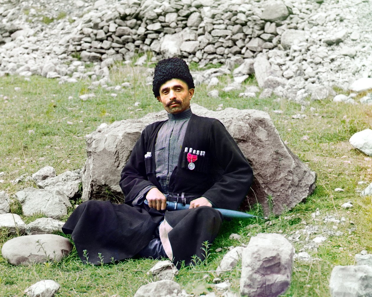 Dagestani-typer - Sunnimuslimsk mann i tradisjonell kjole og hodeplagg, med en dolk med skjede ved siden, sitter på bakken, det russiske imperiet, mellom 1905 og 1915 av Sergey Prokudin Gorsky