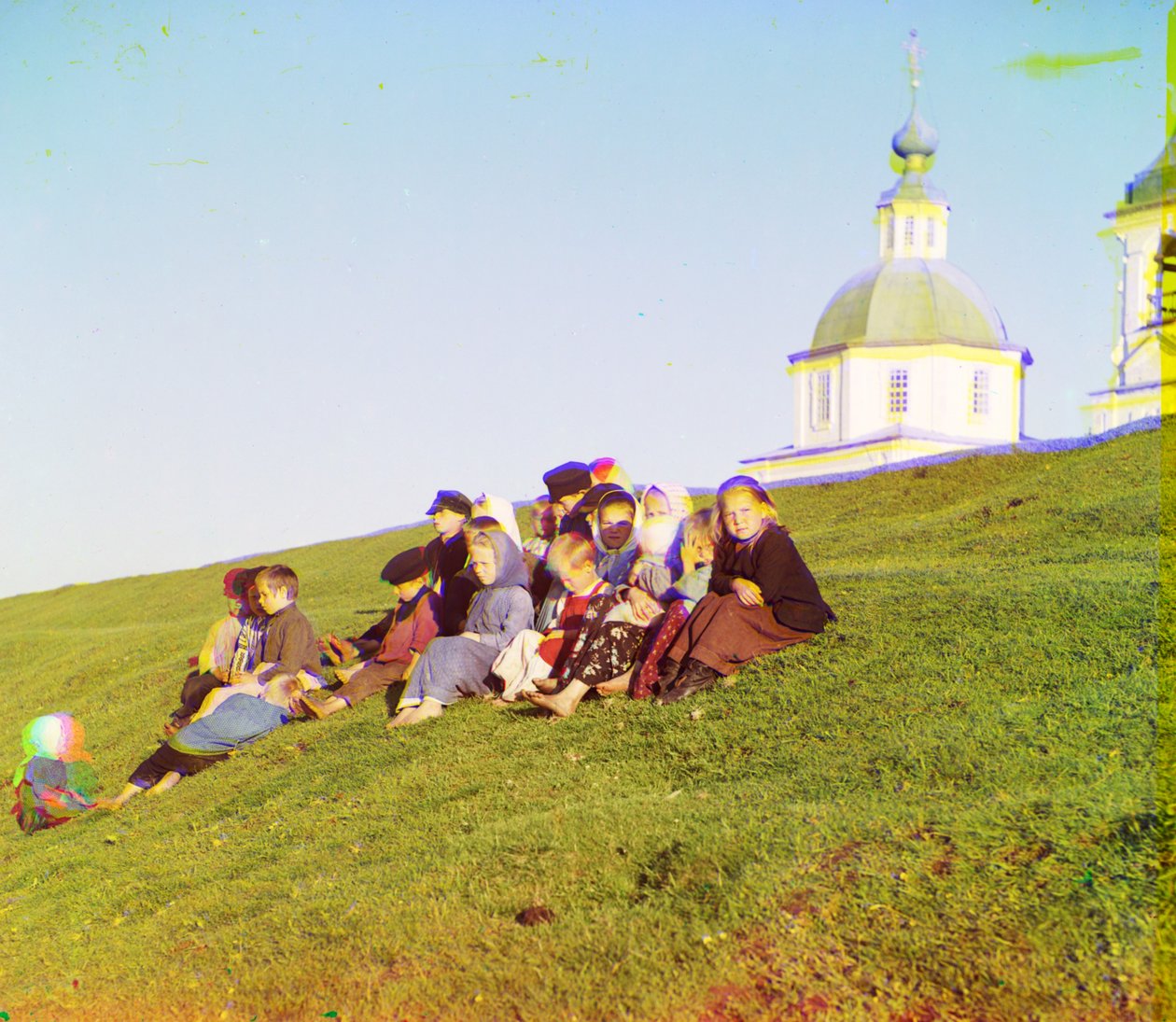 Russiske barn sitter på siden av en ås nær en kirke og klokketårn på landsbygda nær White Lake, nord i det europeiske Russland, 1905-1915 av Sergey Prokudin Gorsky