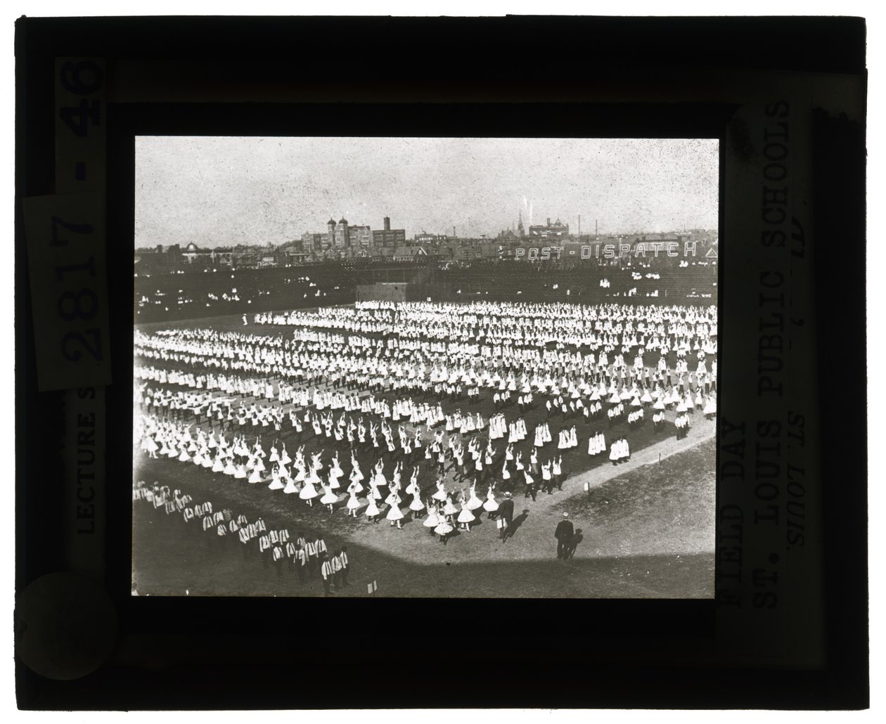 Horisontalt, svart -hvitt foto av hundrevis av skolebarn som stilte opp i formasjon til Field Day -parade og -konkurranse. Alle jentene i hvite kjoler og guttene i hvite skjorter og slips med mørke bukser av Unbekannt Unbekannt