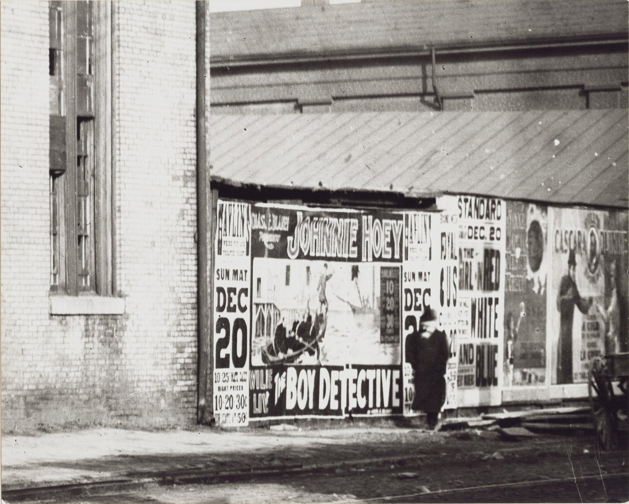 En mann går forbi en vegg med plakatannonser, inkludert en for Johnnie Hoey The Boy Detective som spiller på Havlins teater på 600 Walnut Street. av Unbekannt