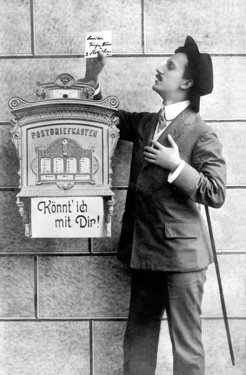 En elegant mann i dress, hatt og stokk, legger ut en lapp i en postkasse. Tyskland rundt 1920 Historisk fotografi, mann ved siden av en postkasse, rundt 1920 av Unbekannt